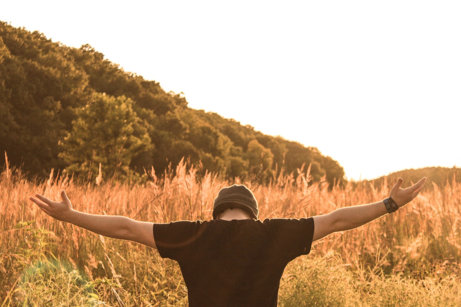 View from behind of a man standing in a wheat field with his head bowed and arms spread open