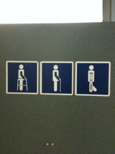 Photo of a sign in a restroom where one of the figures on the sign appears to have a tail