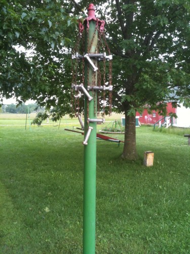 Photo of a pole that resembles a tetherball pole, but with metal chains and bars instead of a tetherball