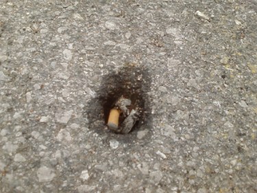 Photo of a hole in the pavement with a cigarette butt laying inside