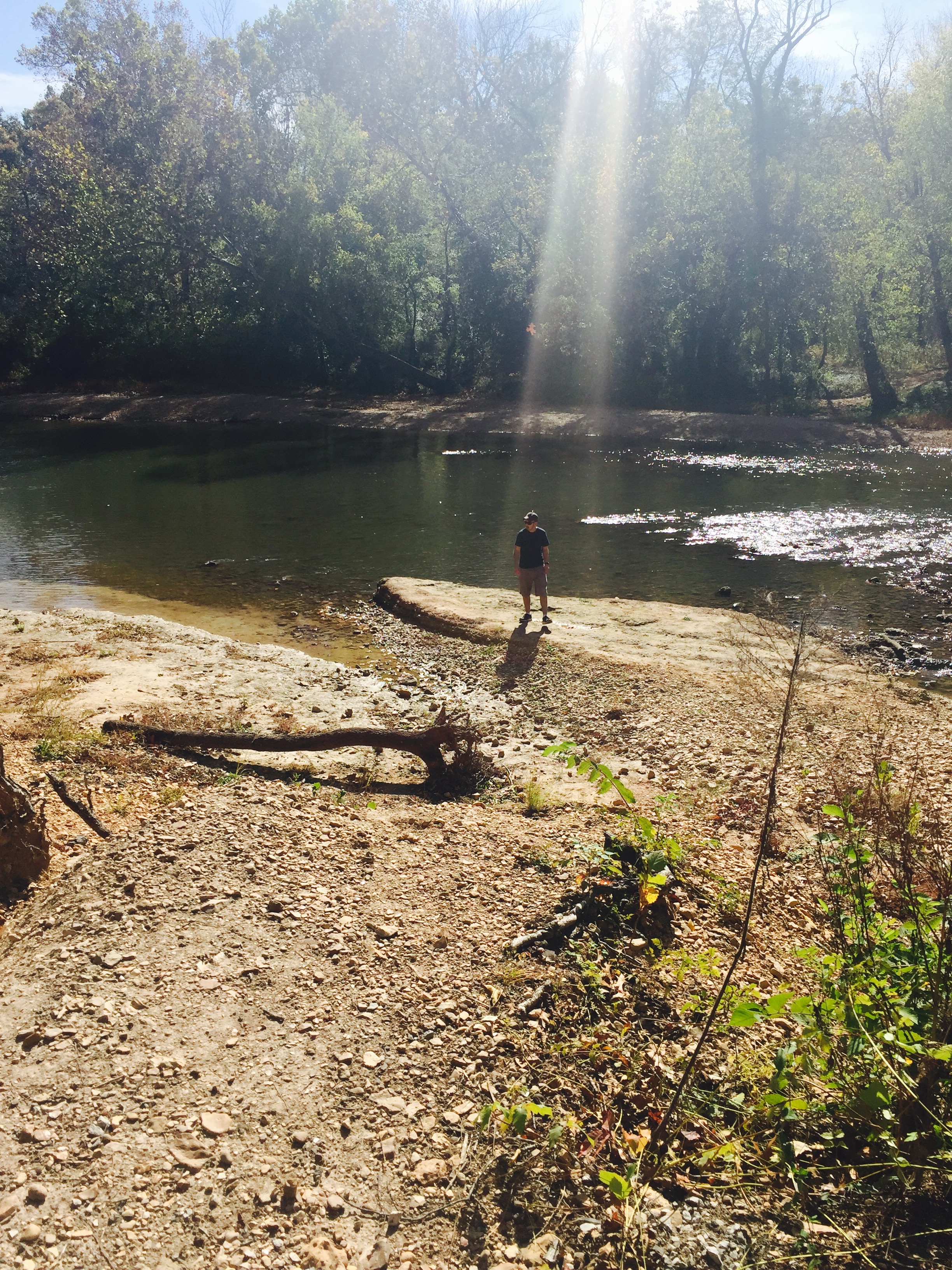 Tim standing on rocks by the creek with a ray of sunshine shining down on him